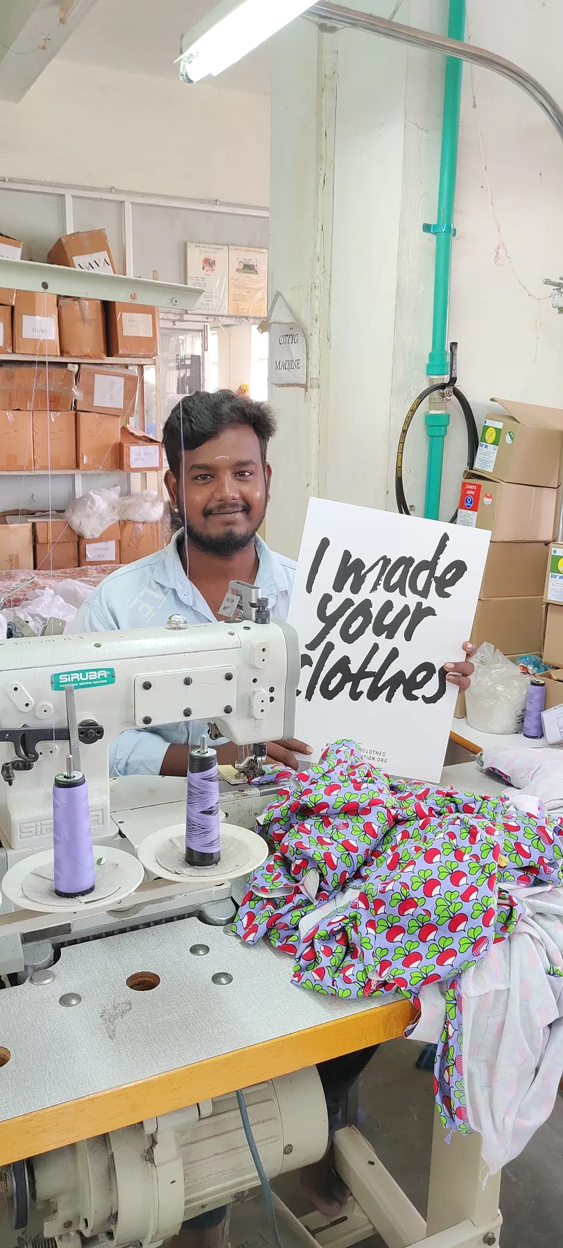Macrofast tailor at his sewing machine holding an I made your clothes sign